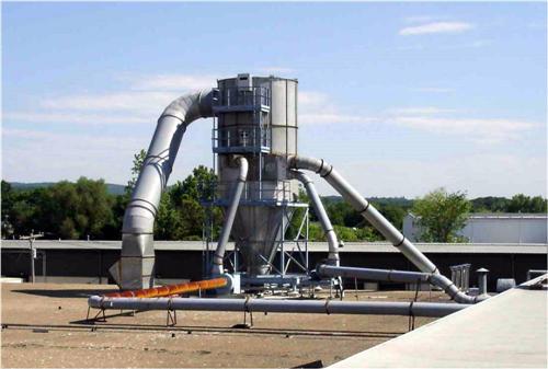 Cyclone dust collector system with ductwork installed on a rooftop, photographed against a blue sky.